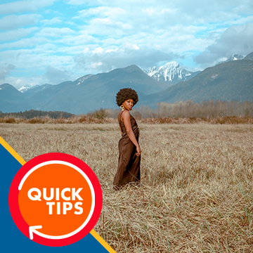 Woman in a brown dress standing in a golden field with mountains behind her, demonstrating a bright and beautiful color grade in Photoshop