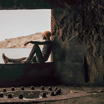 Person sitting in a window opening of a ruined concrete structure overlooking the coast, demonstrating Lightroom controls and Adobe Camera Raw edits