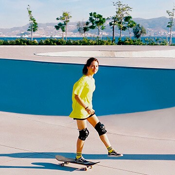 Person in a yellow shirt riding a skateboard at a skate park by the coast, showing a total image makeover in Photoshop