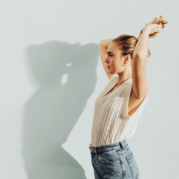Backlit portrait of a woman with her arm raised, casting a dramatic shadow on a white wall, demonstrating shadows created from scratch in Photoshop