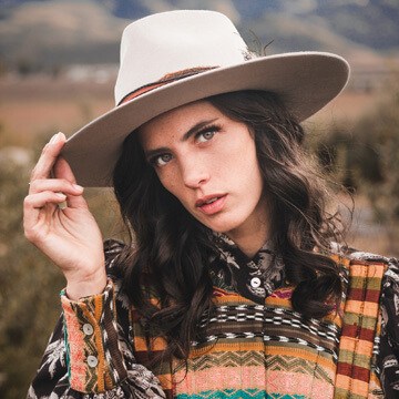 Woman in a patterned poncho and white hat posing against a mountain landscape, thumbnail for a tutorial on enhancing the subject and background separately in Lightroom Desktop