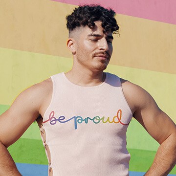 Man in a tank top reading 'be proud' composited against a rainbow-striped background, thumbnail for a tutorial on combining photos and graphics in Photoshop