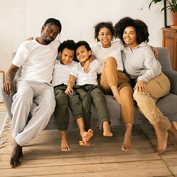 Family of five sitting together on a couch smiling, thumbnail for a tutorial on swapping faces in Photoshop using AI Generative Fill
