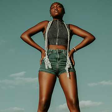 Woman in a striped crop top and denim posing against a teal sky, thumbnail for a tutorial on using Generative Remove in Lightroom Classic