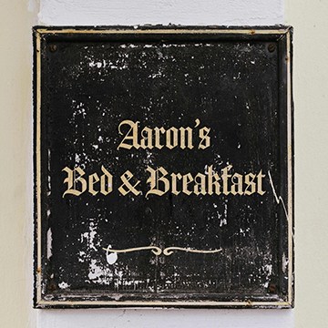 Vintage sign reading 'Aaron's Bed & Breakfast' in ornate serif lettering, thumbnail for a tutorial on matching fonts from images in Photoshop