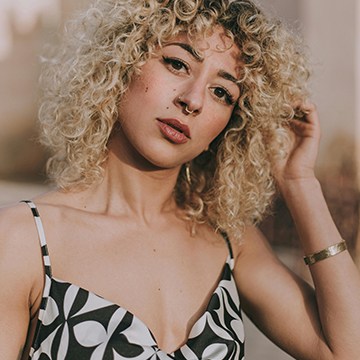 Close-up portrait of a woman with curly blonde hair, thumbnail for a tutorial on removing tattoos using AI in Photoshop