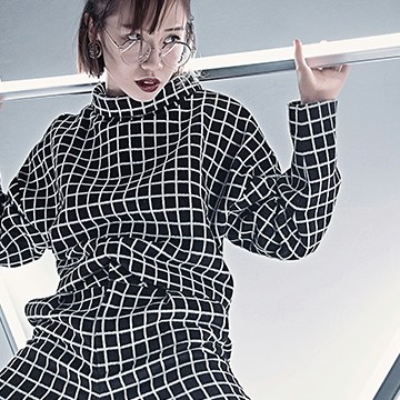Woman with a dark bob and glasses wearing a black-and-white checkered outfit under dramatic lighting, thumbnail for a tutorial on sharpening images in Photoshop