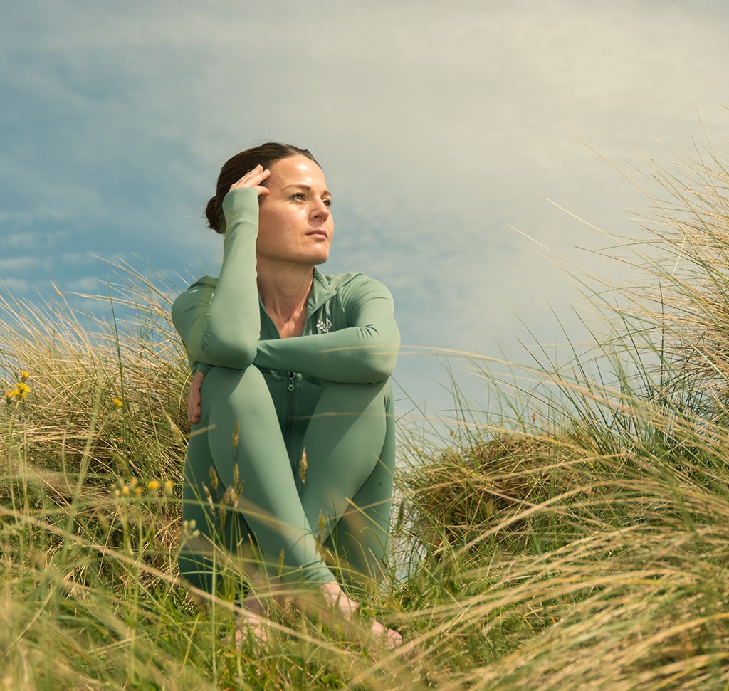 A woman sitting in windswept dune grass under a hazy sky, with a saved Lightroom Classic preset applied