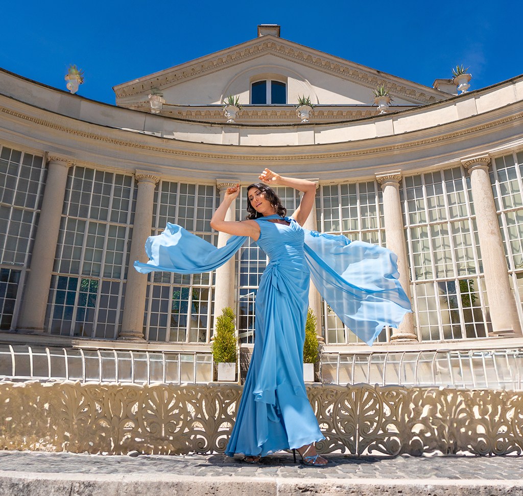 A woman in a flowing sky-blue gown dancing in front of a stone colonnade, edited in Lightroom Classic with distracting objects removed