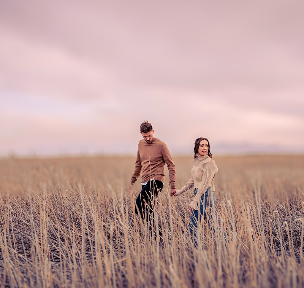 The same couple in a golden grass field with warmer, more vivid tones after an adaptive Lightroom preset.