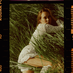 A woman in a white lace dress lying in tall grass inside a film frame