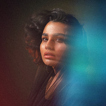 A close-up portrait of a woman with curly hair lit by a teal and orange glow — How to Create an Aura Effect in Photoshop tutorial thumbnail