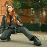 A woman in a leather jacket crouching in a park