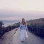 A woman in a white skirt on a coastal path at dusk