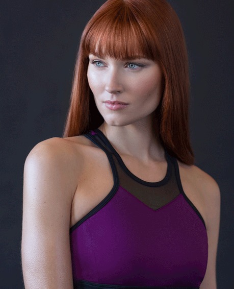 Woman with red hair in a purple top against a dark studio wall