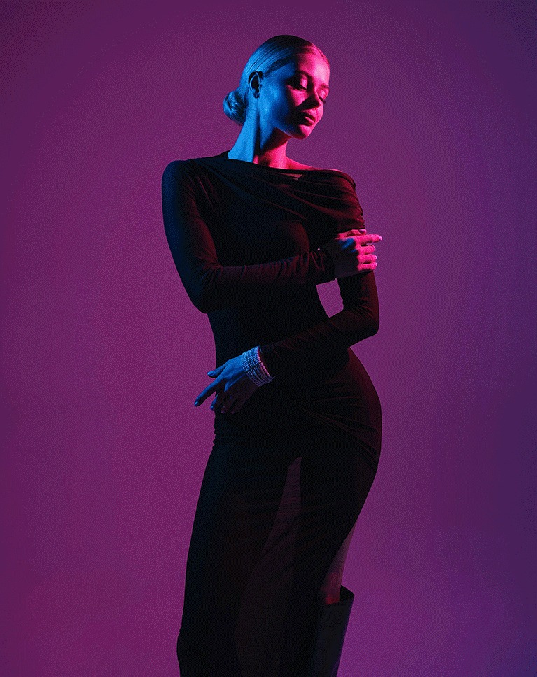 Model in black posed against a flat magenta backdrop