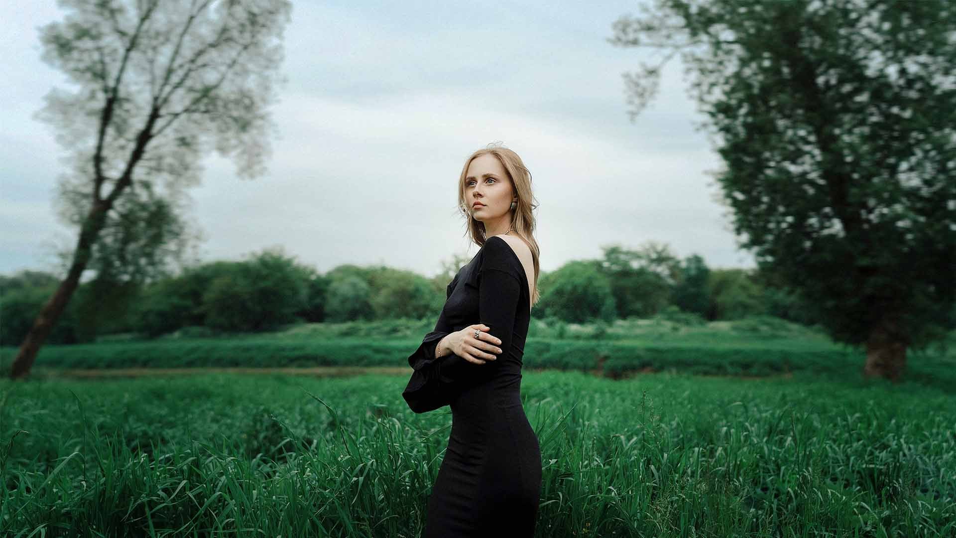 A woman in a black dress standing in a green field, edited in Photoshop with the new Light adjustment layer