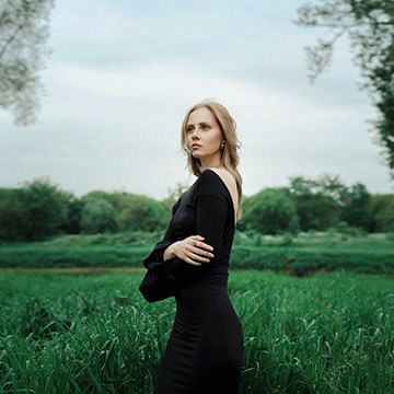 Photoshop Light adjustment layer tutorial thumbnail: a woman in a black dress in a green field