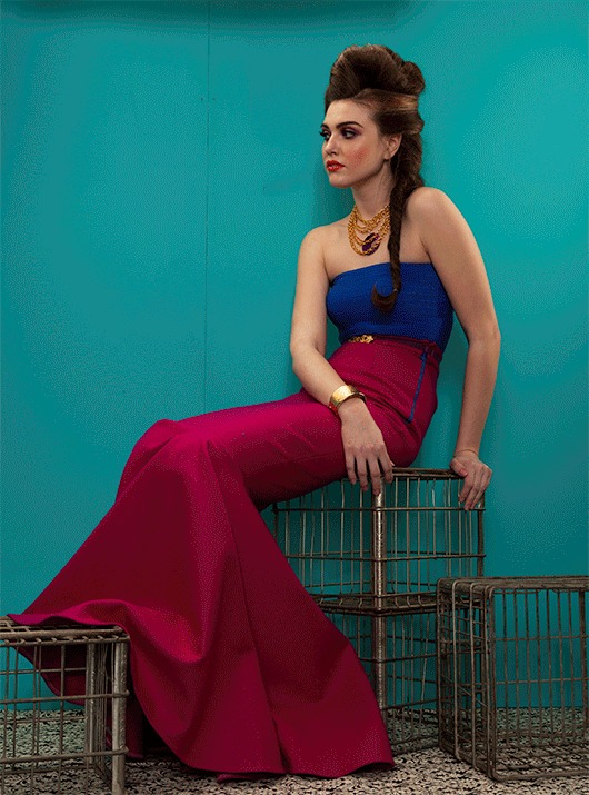 Woman in a magenta gown seated against a teal studio wall