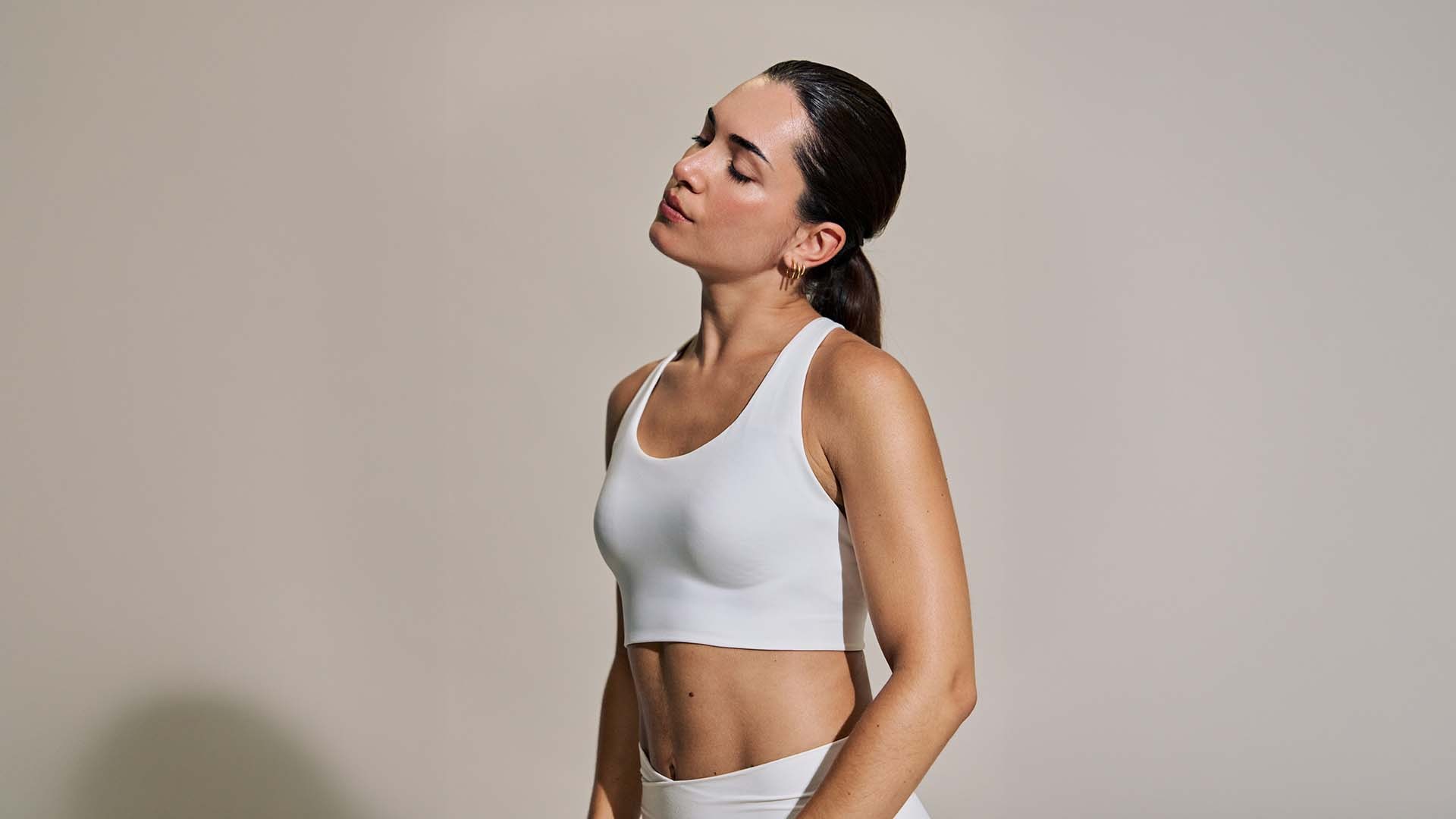 A profile portrait of a woman in a white tank top with her eyes closed and hair pulled into a low ponytail, retouched with Camera Raw's one-click Blemish removal tool