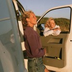 Two women leaning out of a van door at sunset