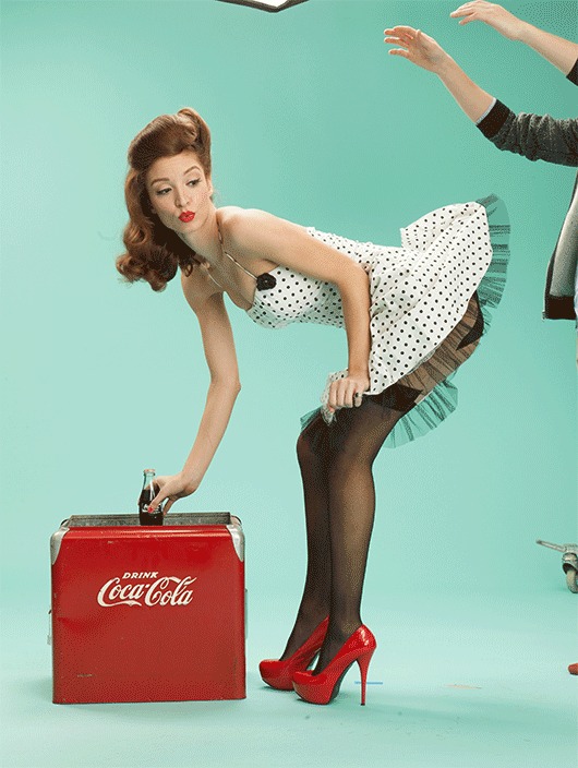 Model in a retro pin-up pose leaning on a red crate against a mint green wall