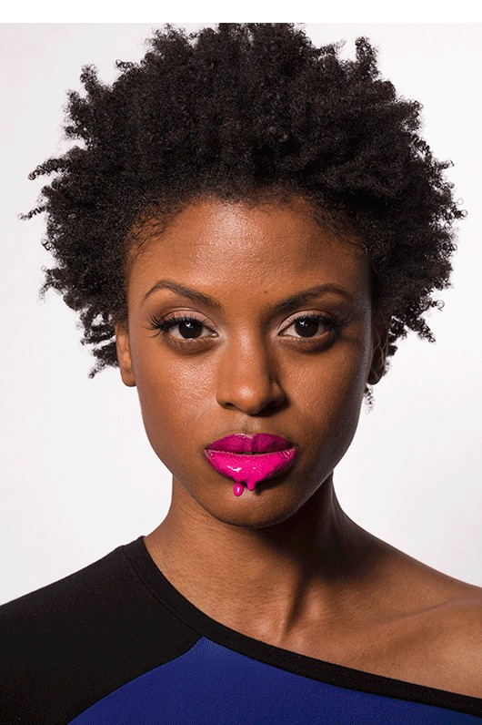 Portrait of a woman with an afro and magenta lipstick on a dark background