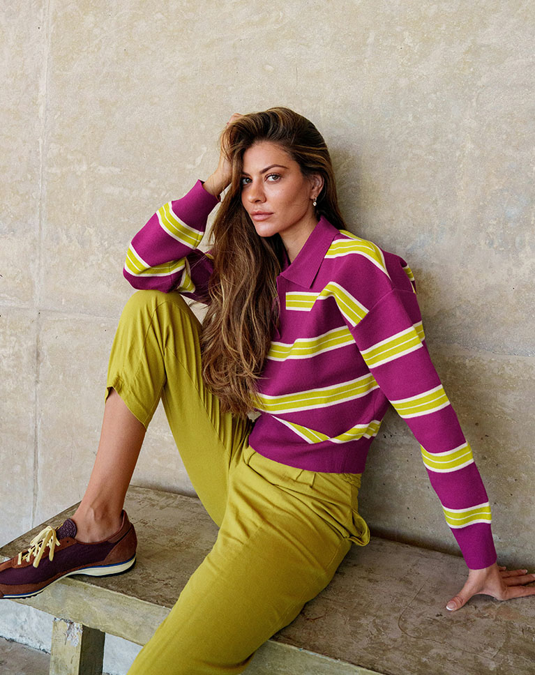 A woman in a magenta and yellow striped shirt sitting on a bench against a concrete wall