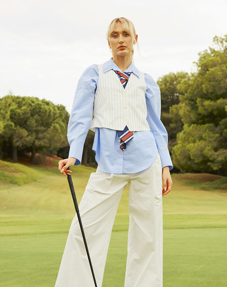 A woman in a white vest holding a golf club on a golf course