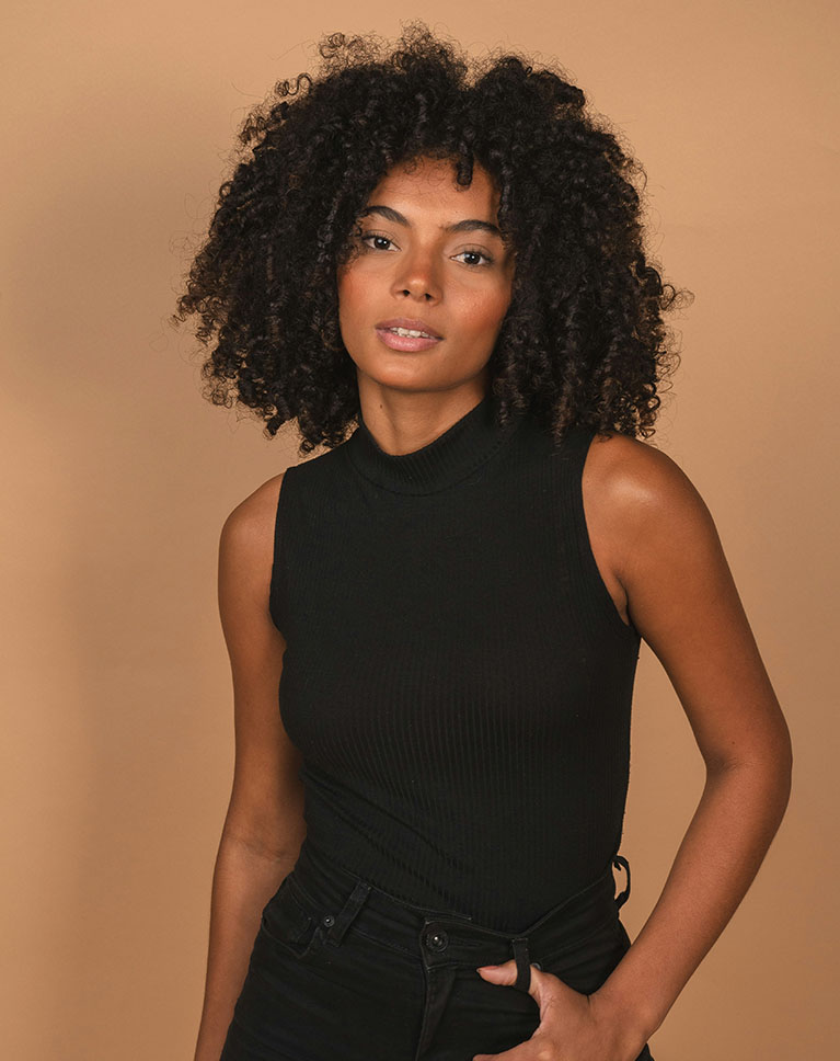 A woman with curly hair photographed on a tan background