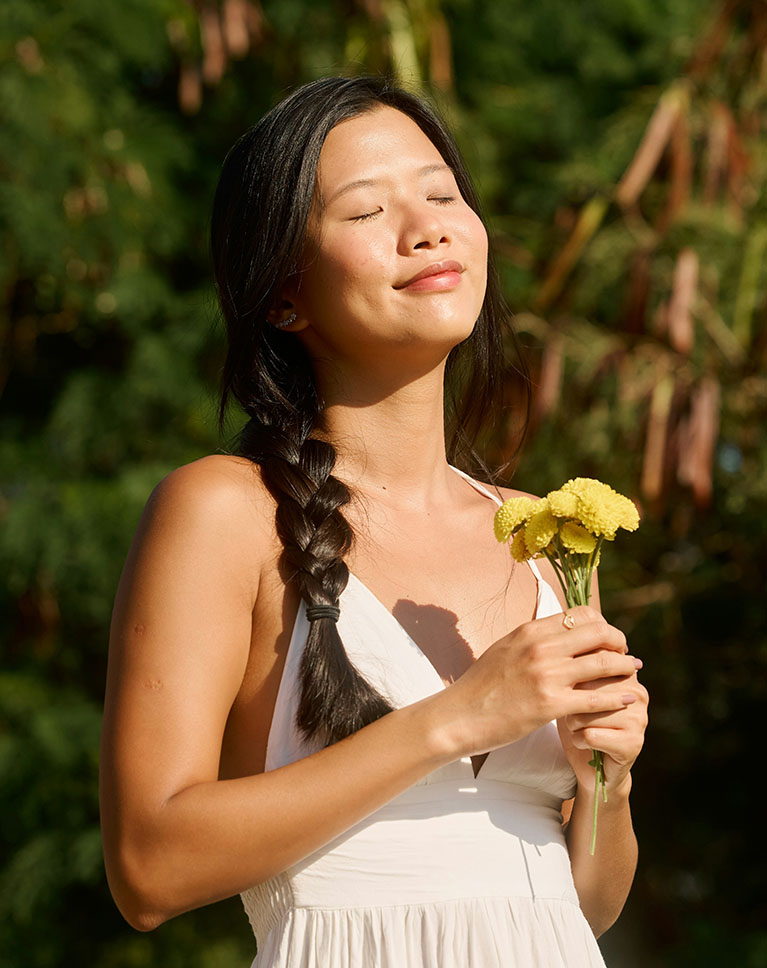 A woman with a long braid holding yellow flowers in front of dense green foliage