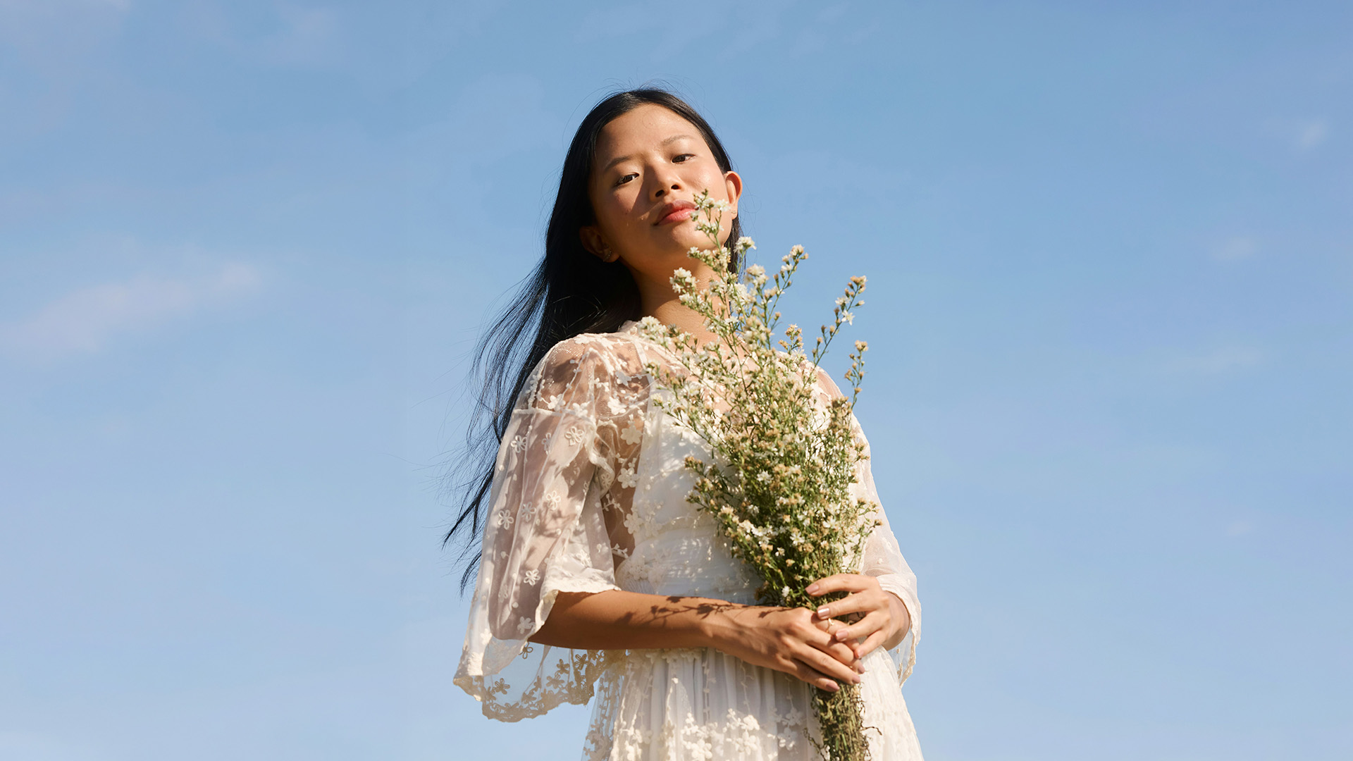 Woman in a white lace dress holding wildflowers against a blue sky, the cutout example from The Ultimate Guide to Selections and Masking in Photoshop