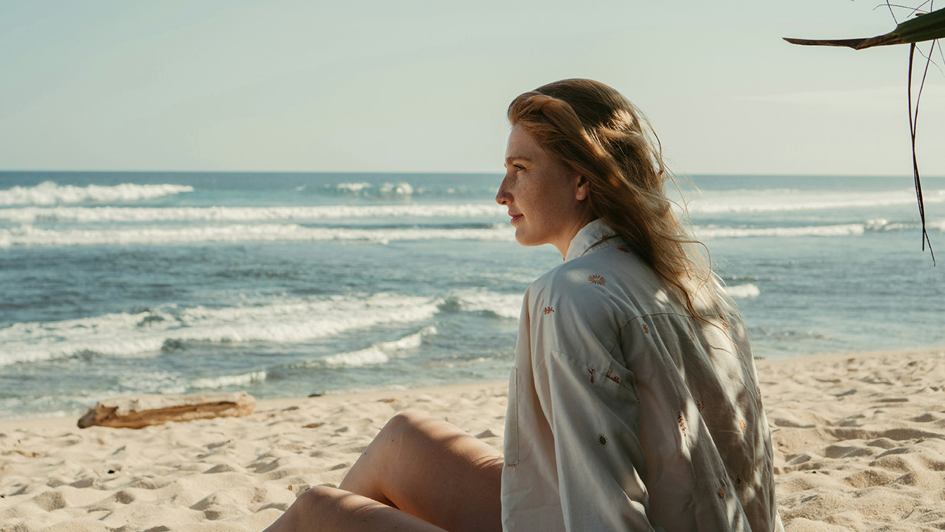 A woman sitting on a beach with a log and a stray branch in the frame