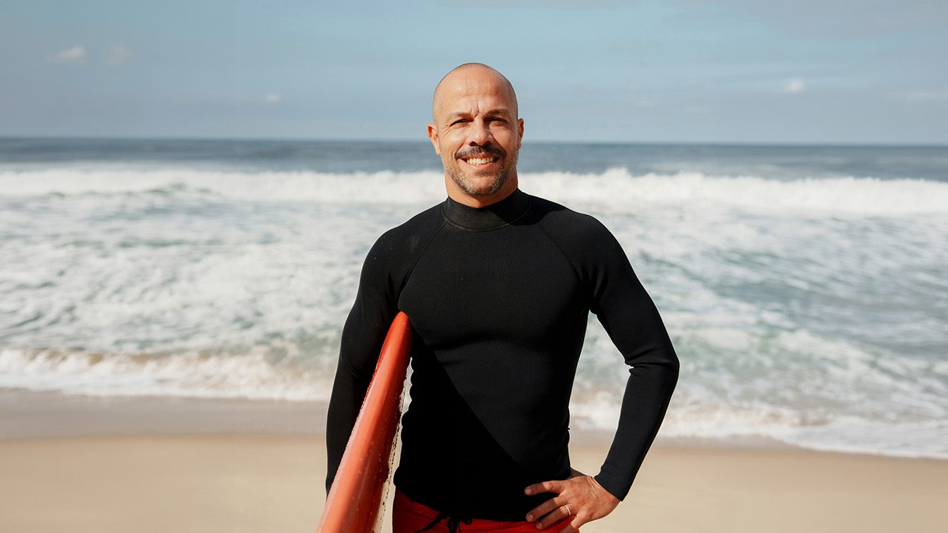 A surfer in a black wetsuit holding a red surfboard on the beach