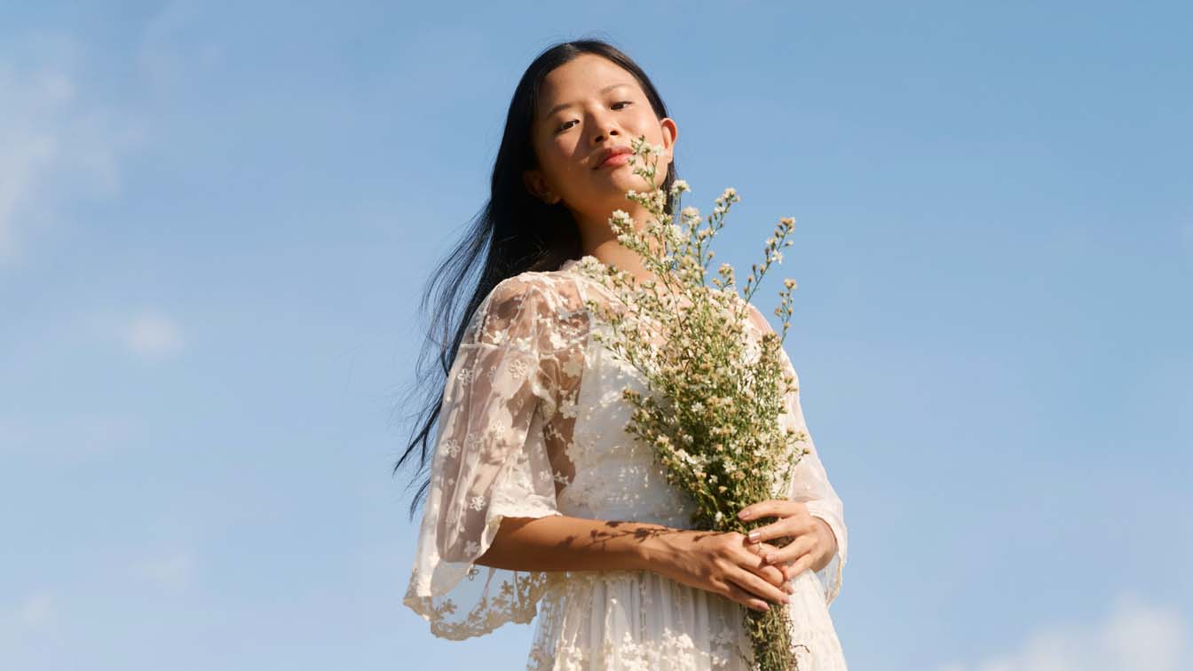 A woman in a lace dress holding wildflowers against a blue sky