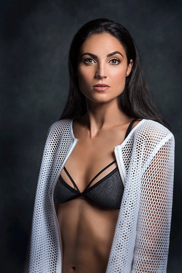 Woman in a black bikini top and white lace jacket against a dark background
