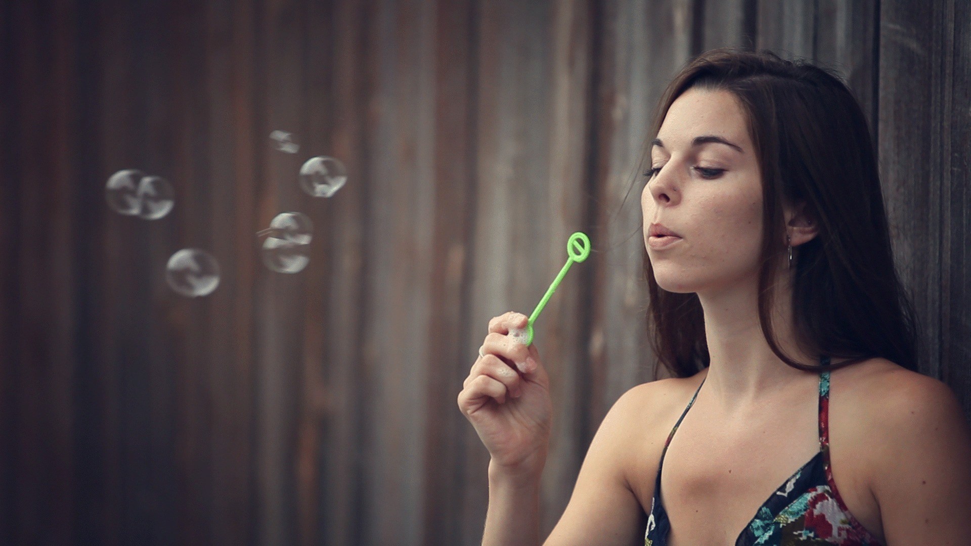 Woman blowing a stream of soap bubbles in front of a dark wooden wall