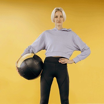 Blonde woman in a gray hoodie posing against a yellow background, demonstrating simple object removal in Photoshop