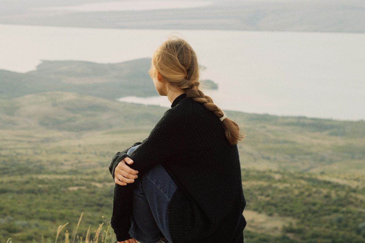 A woman sitting on a rock above a green valley before adjusting Curves and Hue/Saturation