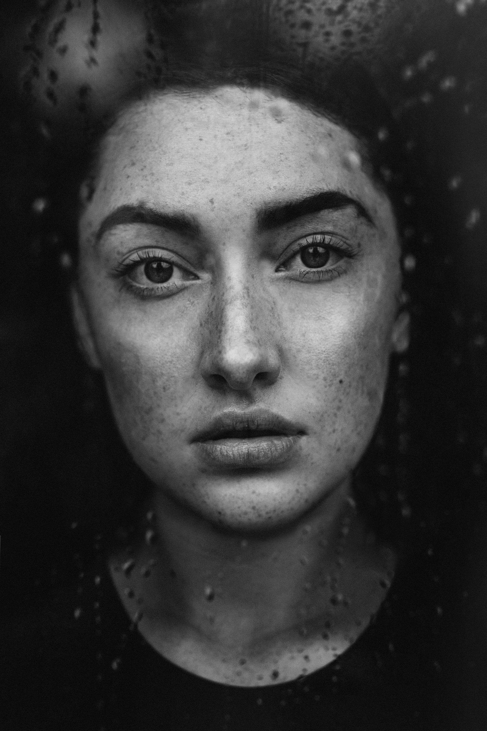 Black-and-white close-up of a woman's face behind a glass covered in water droplets