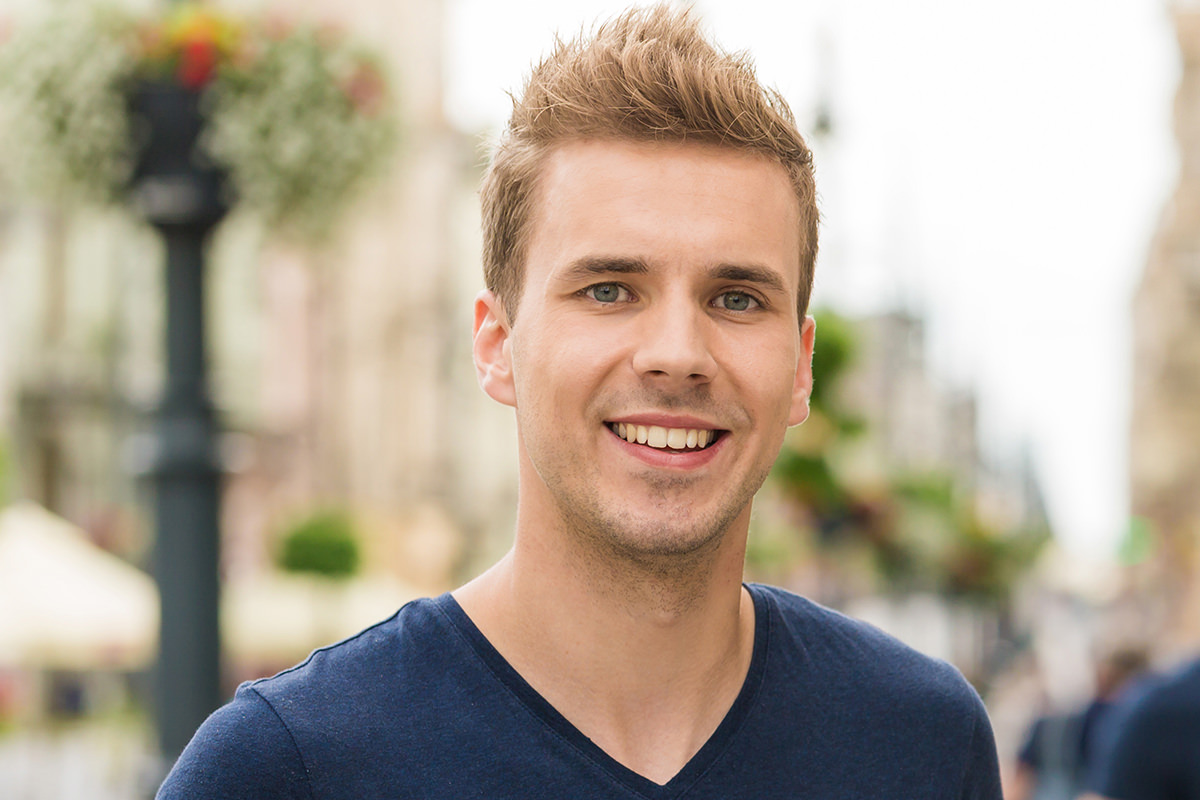 Smiling man in a navy t-shirt on a busy street, before cutting out his hair with the Brush tool