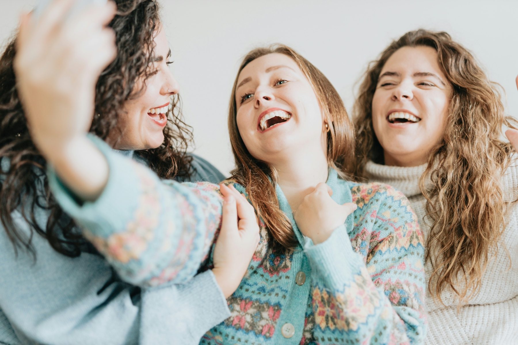Three friends laughing on a couch, the woman on the right with her eyes shut mid-laugh