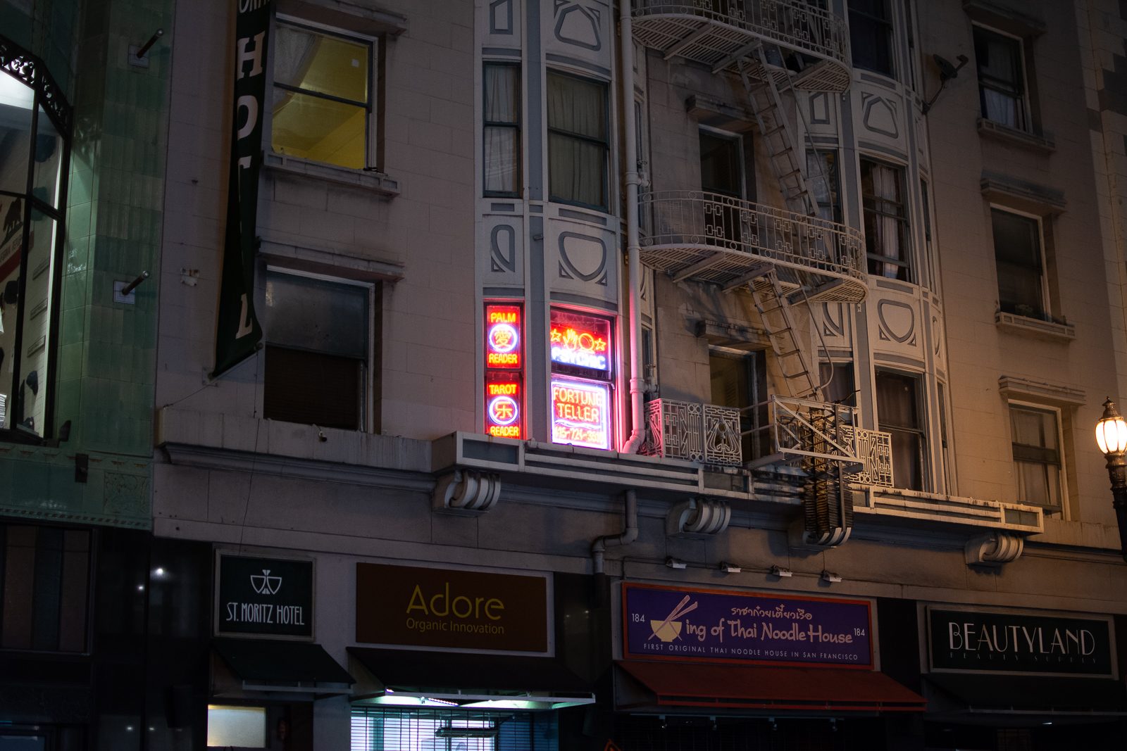 Marcus Soriano photo, before editing: unedited version of the shot: the fortune teller's neon window signs on a dim San Francisco facade at night, a streetlight at right
