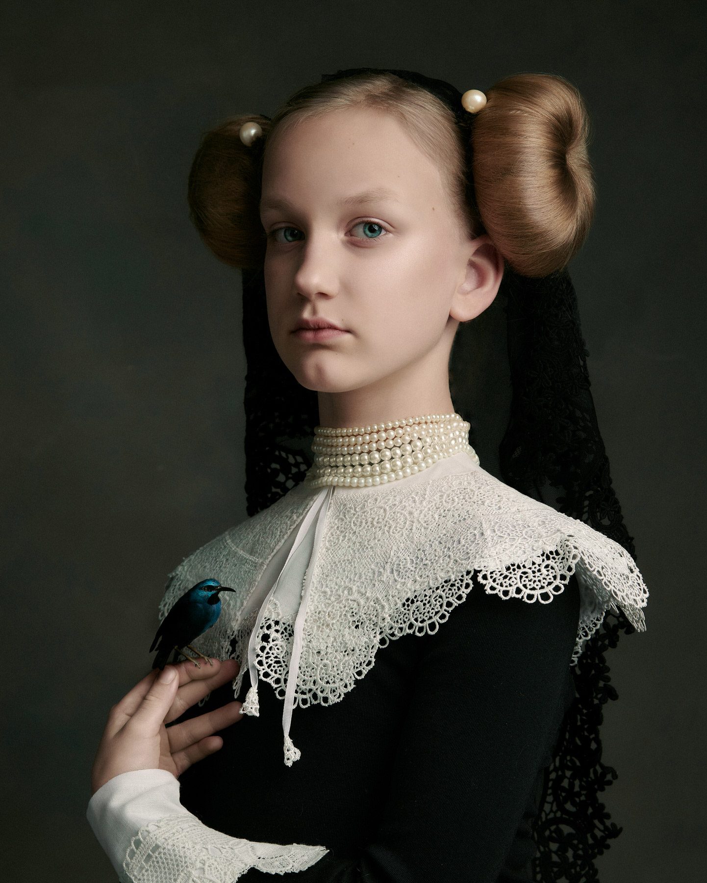 Rembrandt photography: Old Master style portrait of a girl with twin hair buns, pearls and a lace collar, a small blue bird on her hand