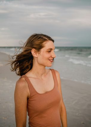 Woman in a tank top smiling on a windy beach