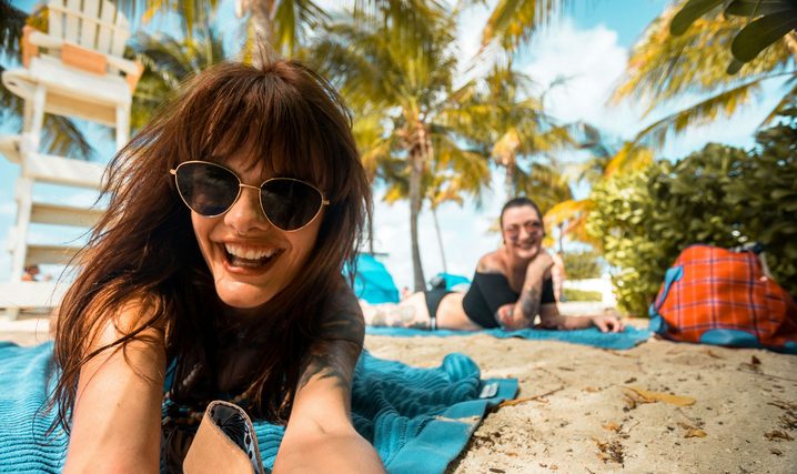 Two women in sunglasses lying on towels under palm trees
