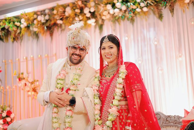 Smiling bride and groom in garlands at a decorated stage