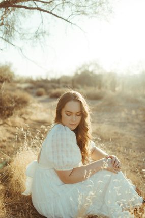 Woman in a white dress sitting in dry grass at sunset
