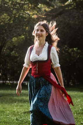 Smiling woman in a dirndl walking across a park lawn