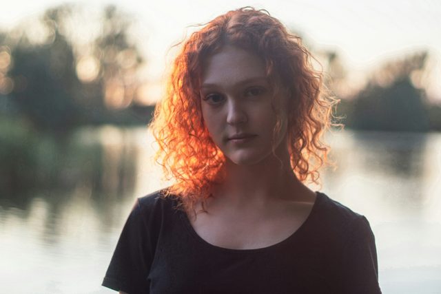 Woman with curly red hair standing by a lake at dusk
